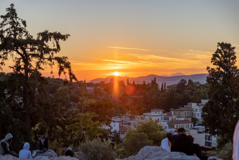 a group of people sitting on a hill with a sunset in the background