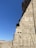 Ancient stone carvings depict figures and hieroglyphics on a wall, set against a clear blue sky. The carvings include detailed representations of human-like figures and intricate symbols.