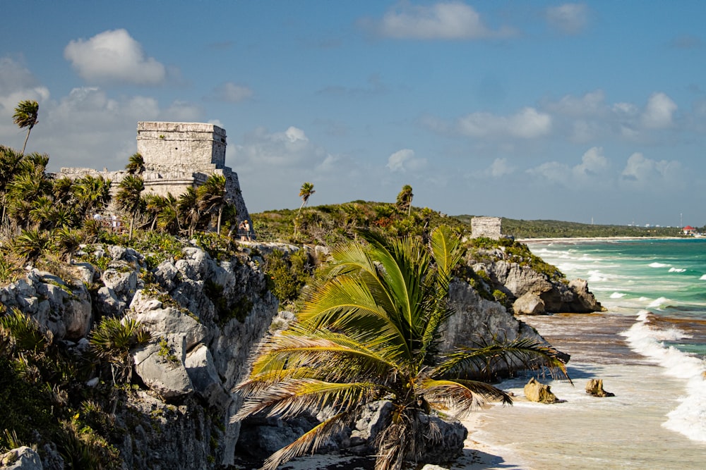 a rocky beach with a castle on it with Tulum in the background