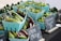 Baskets of fresh green and burgundy okra, along with shishito peppers, are displayed at a market stall. Chalkboard signs in small wooden stands indicate prices for each item. The produce appears fresh and vibrant, arranged neatly in blue containers.