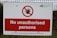 A warning sign is mounted on a wire fence with bold red and white colors, stating 'No unauthorised persons'. There is a prohibition symbol featuring a red circle with a slash over a hand. The logo of the Environment Agency is displayed in the top right corner.