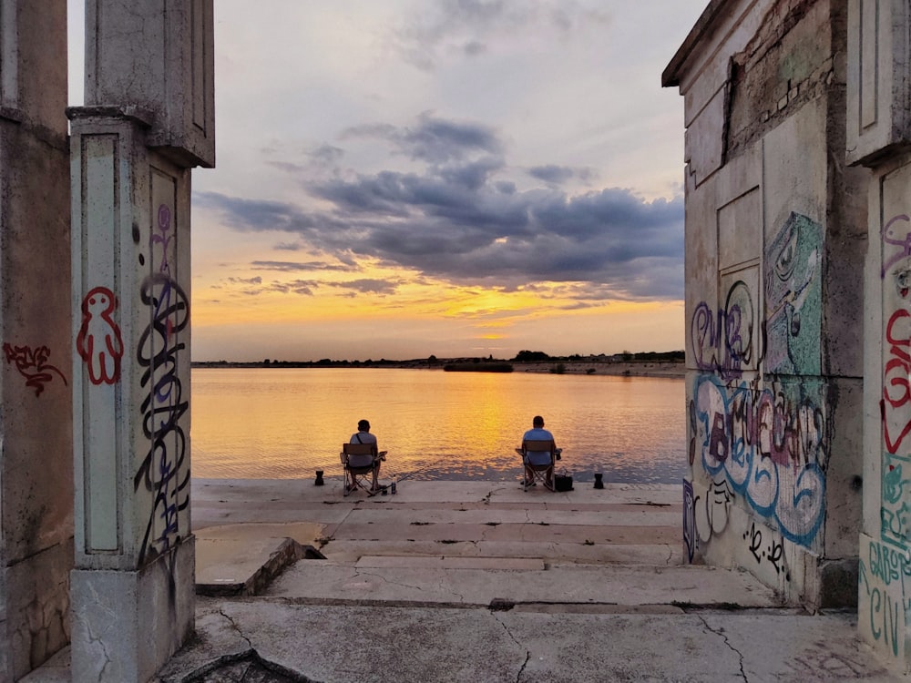 a couple of people sitting on a bench by a body of water