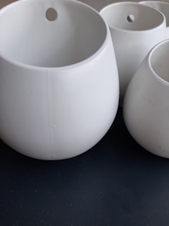 Several white, round, ceramic pots of various sizes are arranged closely together. Each pot has a small hole near the top, possibly for hanging or for drainage.