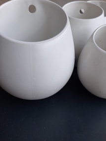 Several white, round, ceramic pots of various sizes are arranged closely together. Each pot has a small hole near the top, possibly for hanging or for drainage.