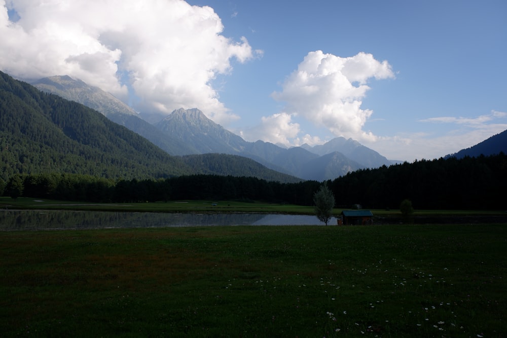 a grassy field with a body of water and mountains in the background