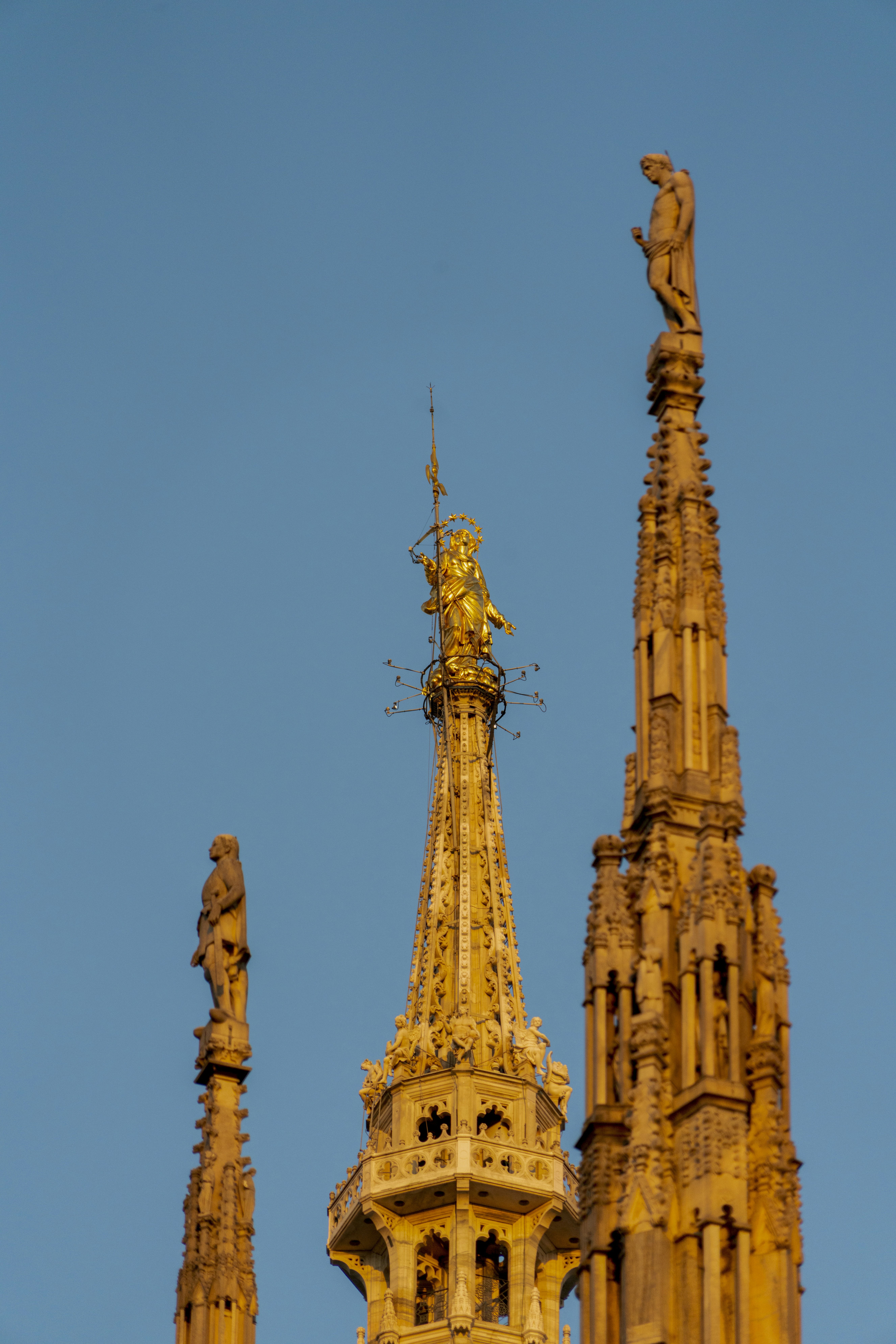 a tall building with a statue on top with Milan Cathedral in the background