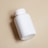 A plain white plastic bottle with a screw-on cap lies on a beige surface, casting a shadow to one side.