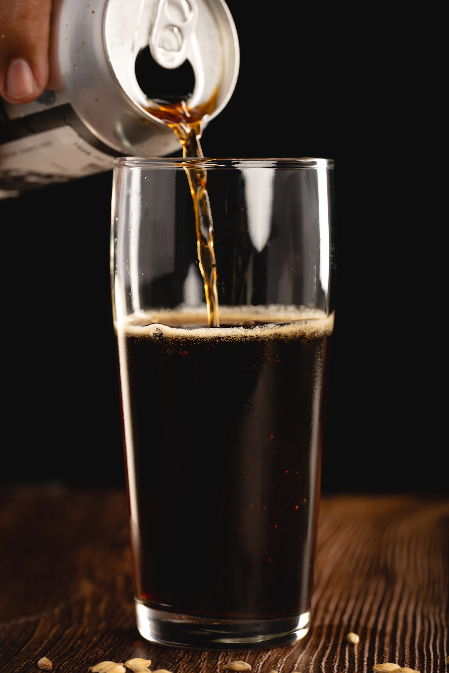 Black oatmeal stout pouring from a can into a pint glass, the tan head rising
