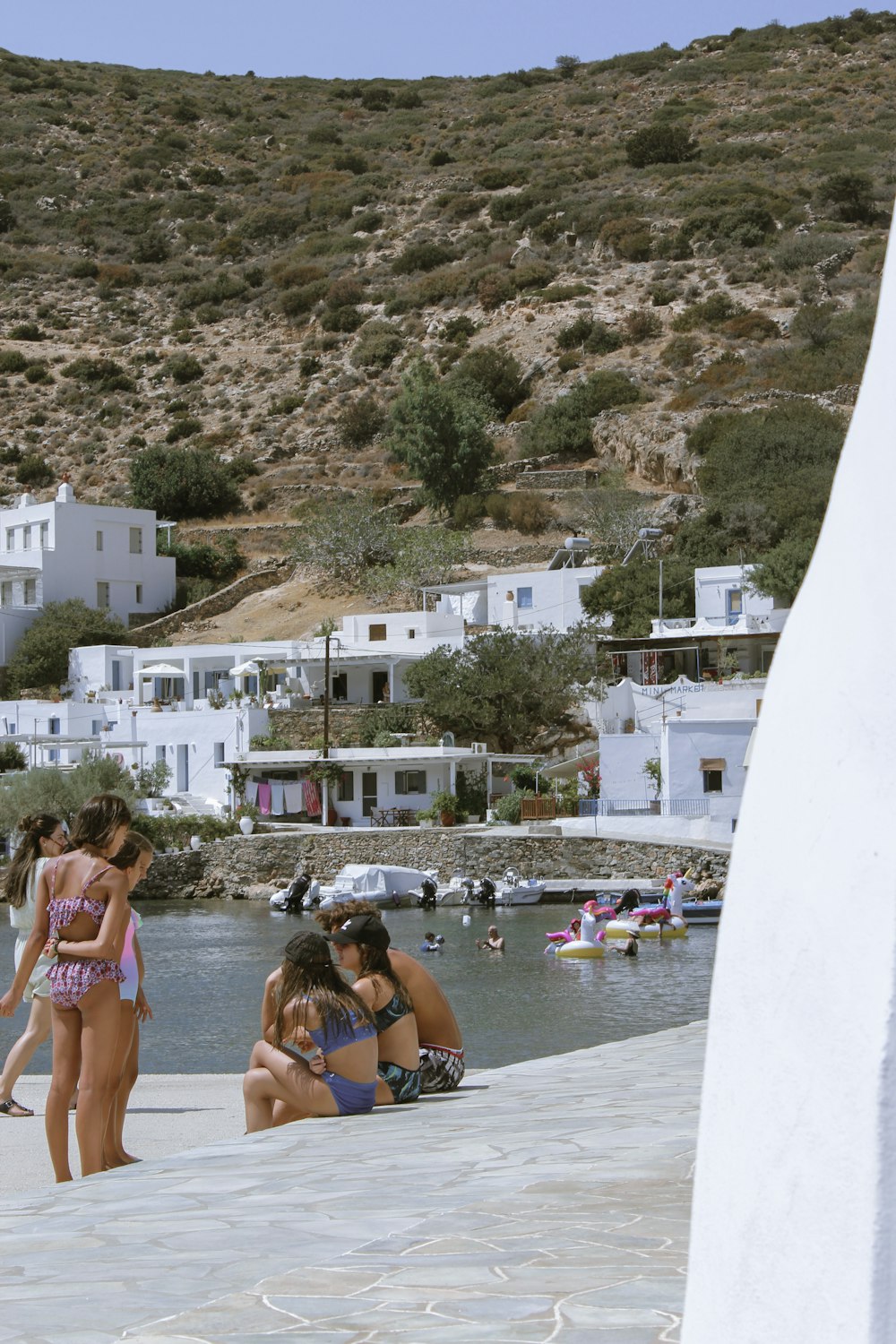 a group of people sitting on a stone walkway by a hill with buildings