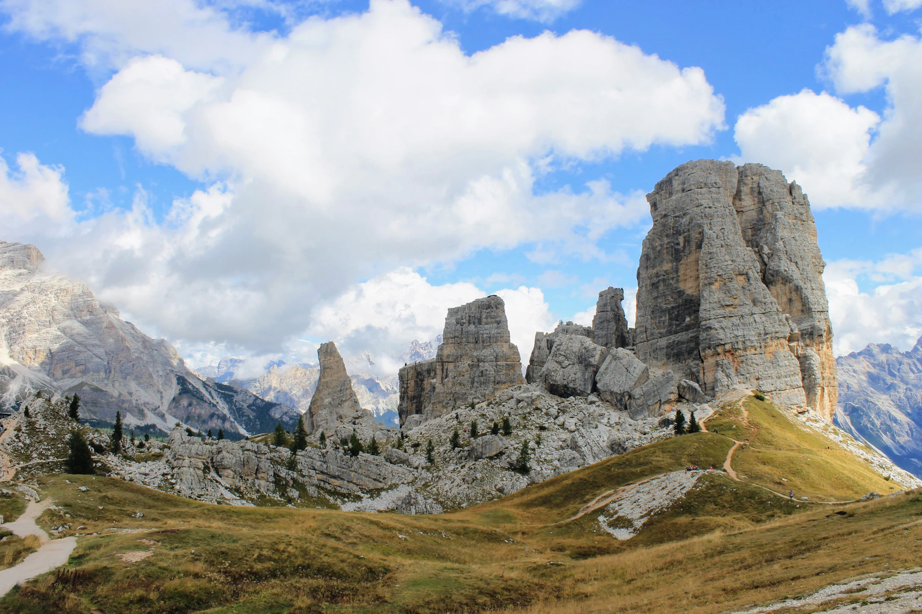 Photograph of Walkers follow pale paths among the separate limestone towers of Cinque Torri.