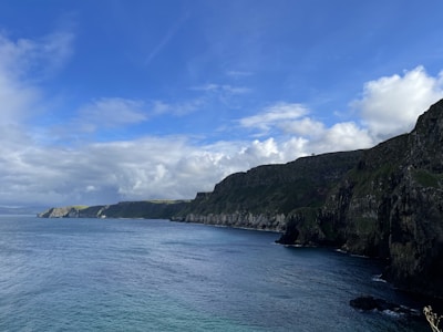 A panoramic view of rugged cliffs meeting the Atlantic Ocean under a cloudy sky.