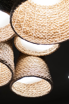 A cluster of woven basket-style lampshades with a natural, textured appearance hanging from above. The lampshades are illuminated, casting warm light and creating a cozy ambiance. The intricate pattern of the weave is clearly visible, showcasing craftsmanship.