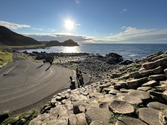 a road next to a body of water with rocks on the side