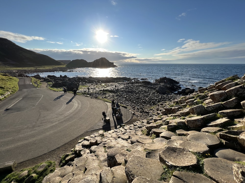 a road next to a body of water with rocks on the side