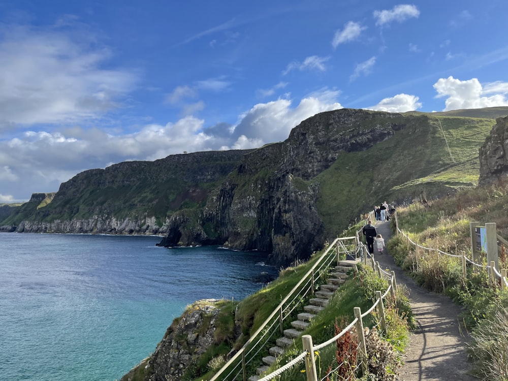 a path next to a body of water with a hill in the background