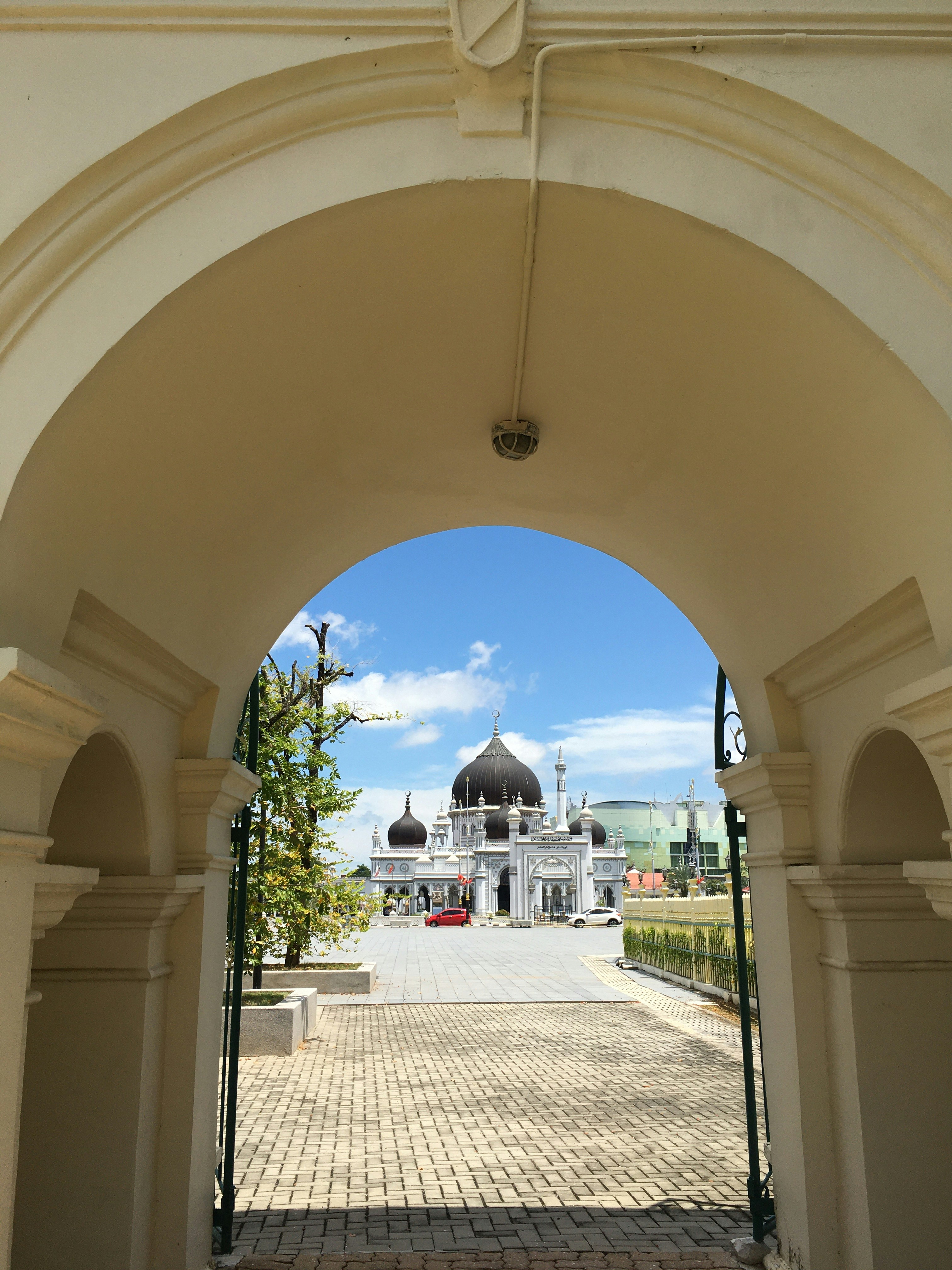 a stone walkway with a stone archway and a building in the background