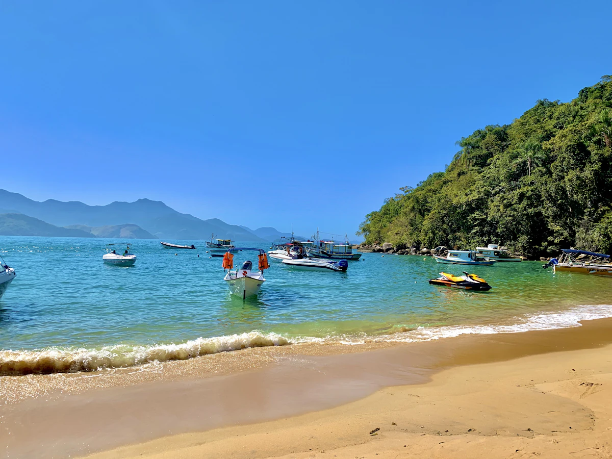 Praia fluvial com barcos de passeio e pessoas aproveitando o dia