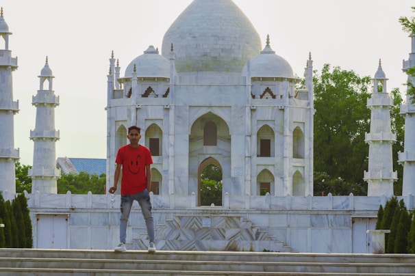 A smiling Sri Lankan student standing in front of Bucharest's iconic architecture, holding travel documents.