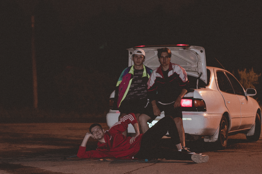 a group of men in clothing by a car at night