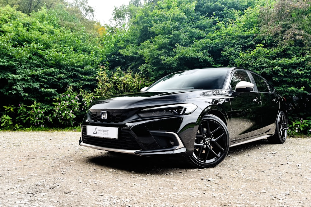 a black car parked on a gravel road with trees in the background