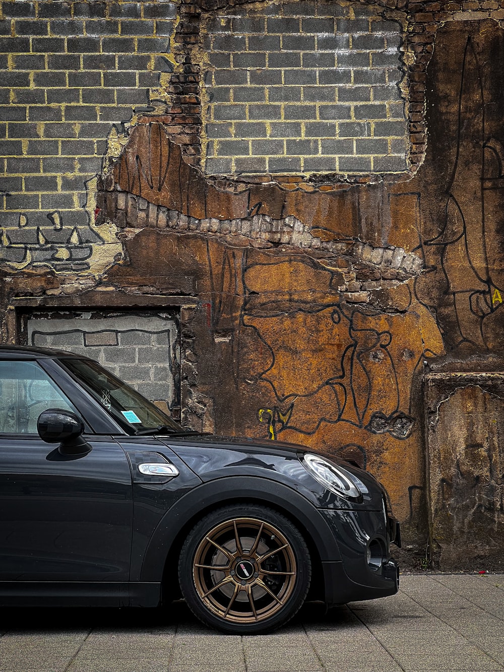 a car parked in front of a brick wall with graffiti on it