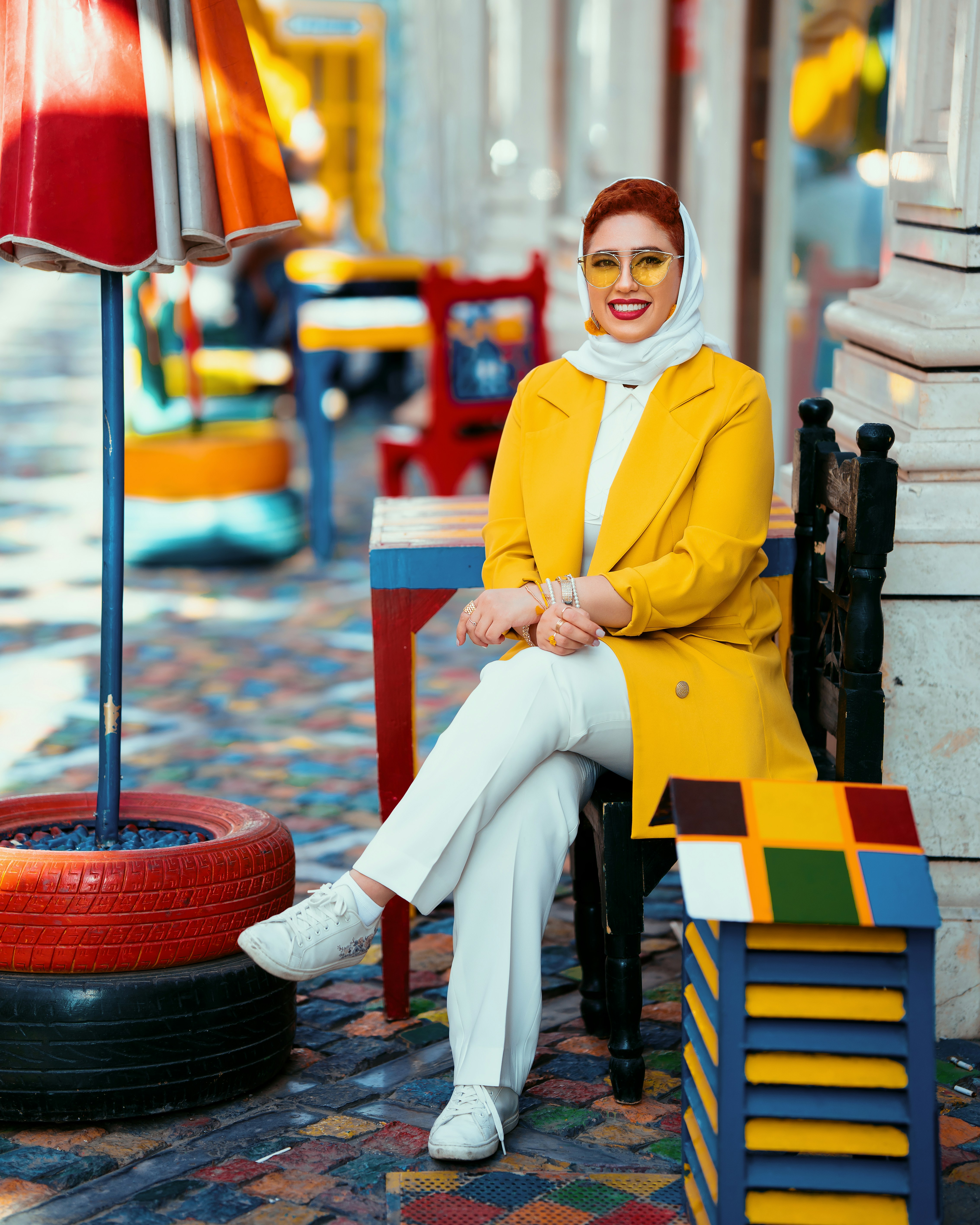 Smiling woman in yellow coat seated in a colorful cafe