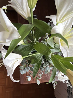 Elegant floral centerpiece with white lilies and greenery on a wooden table