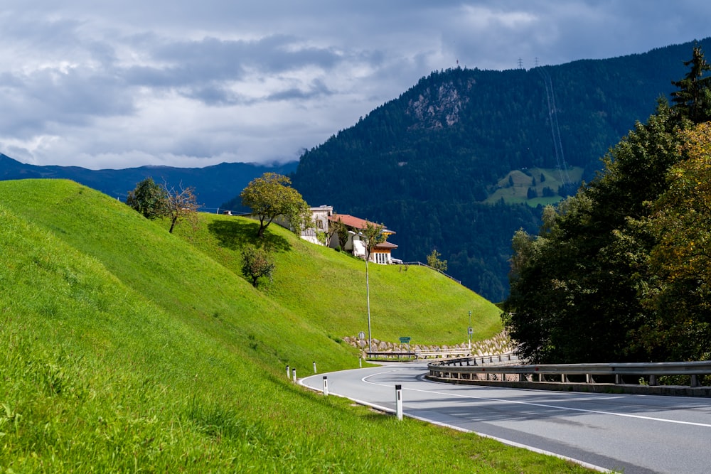 a road leading to a house on a hill with trees and mountains in the background
