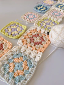 Close-up of hands crocheting a colorful granny square blanket.