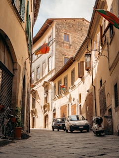 a cobblestone street with cars and buildings on either side of it