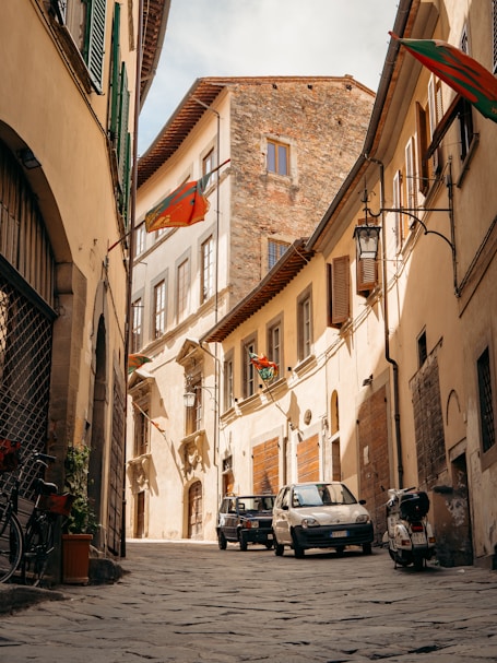 a cobblestone street with cars and buildings on either side of it