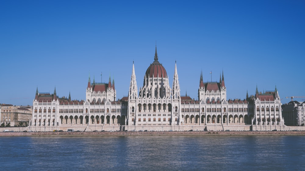 a large white building with towers by a body of water with Hungarian Parliament Building in the background