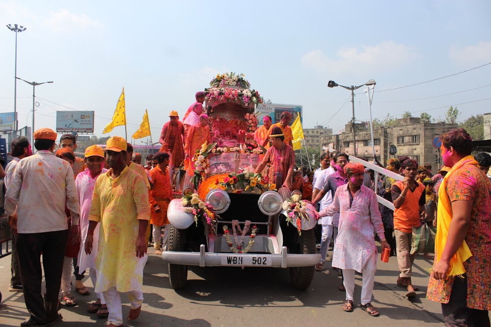 a group of people walking down a street with a car with flowers on it