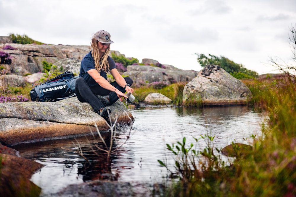 a man sitting on a rock by a body of water