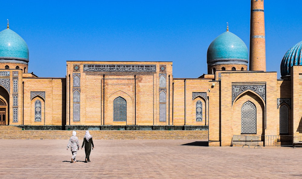 a couple of people walking in front of a building with domed roofs