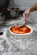a person putting tomato sauce on a pizza