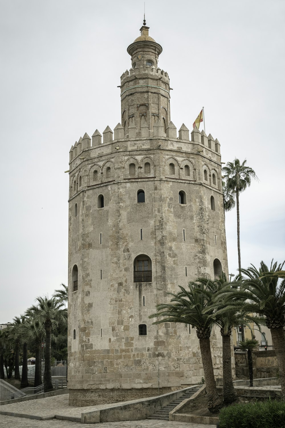 un alto edificio de piedra con palmeras con Torre del Oro al fondo