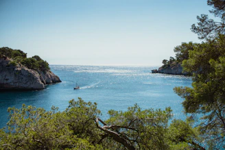A scenic boat sailing over clear blue coastal waters under a bright sky.