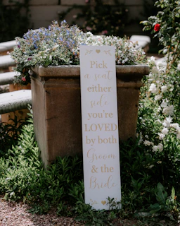 Elegant copper-toned wooden sign displaying a bride and groom’s names surrounded by hand-painted flowers.