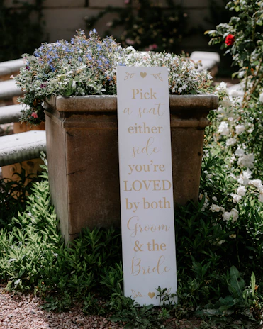 Elegant copper-toned wooden sign displaying a bride and groom’s names surrounded by hand-painted flowers.