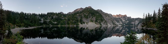 A serene mountain lake reflecting a vibrant sunset sky, framed by towering pine trees.