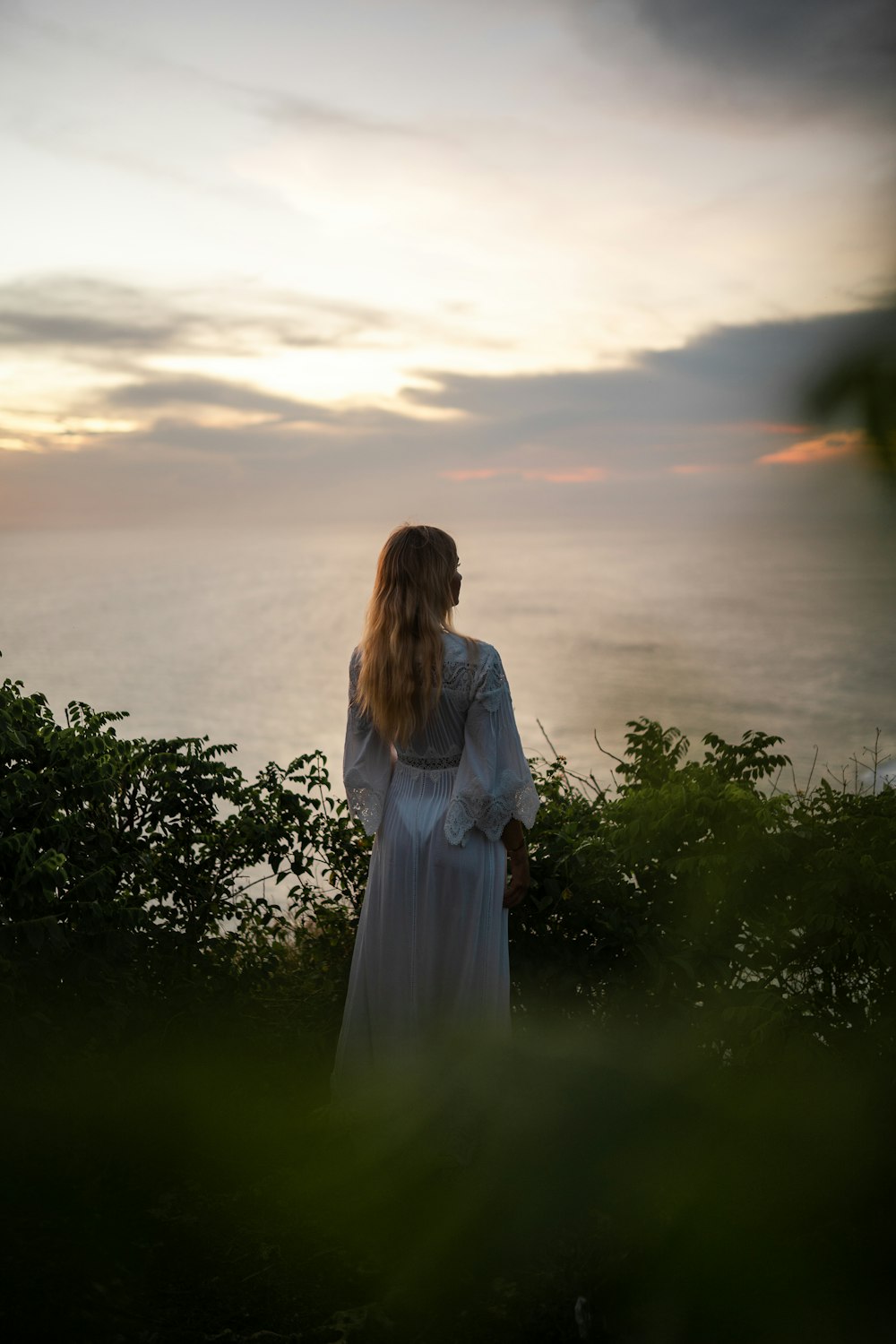 a person in a white dress standing in a field with trees and a sunset