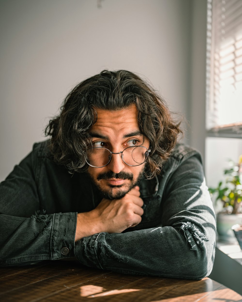 a person with glasses sitting at a table with the hand on the chin