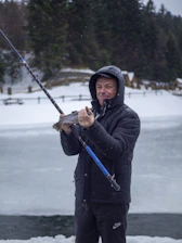 A rugged angler holding a freshly caught northern pike on a misty Swedish lake at dawn.