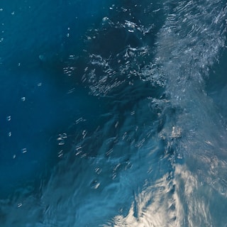 A detailed view of turbulent water, with visible ripples and waves creating a dynamic texture on the surface. The play of light on the water adds a sense of movement and depth.