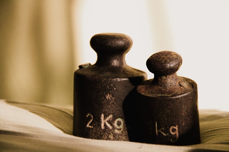 Two vintage iron calibration weights labeled 1kg and 2kg representing mass in the gravitational potential energy formula