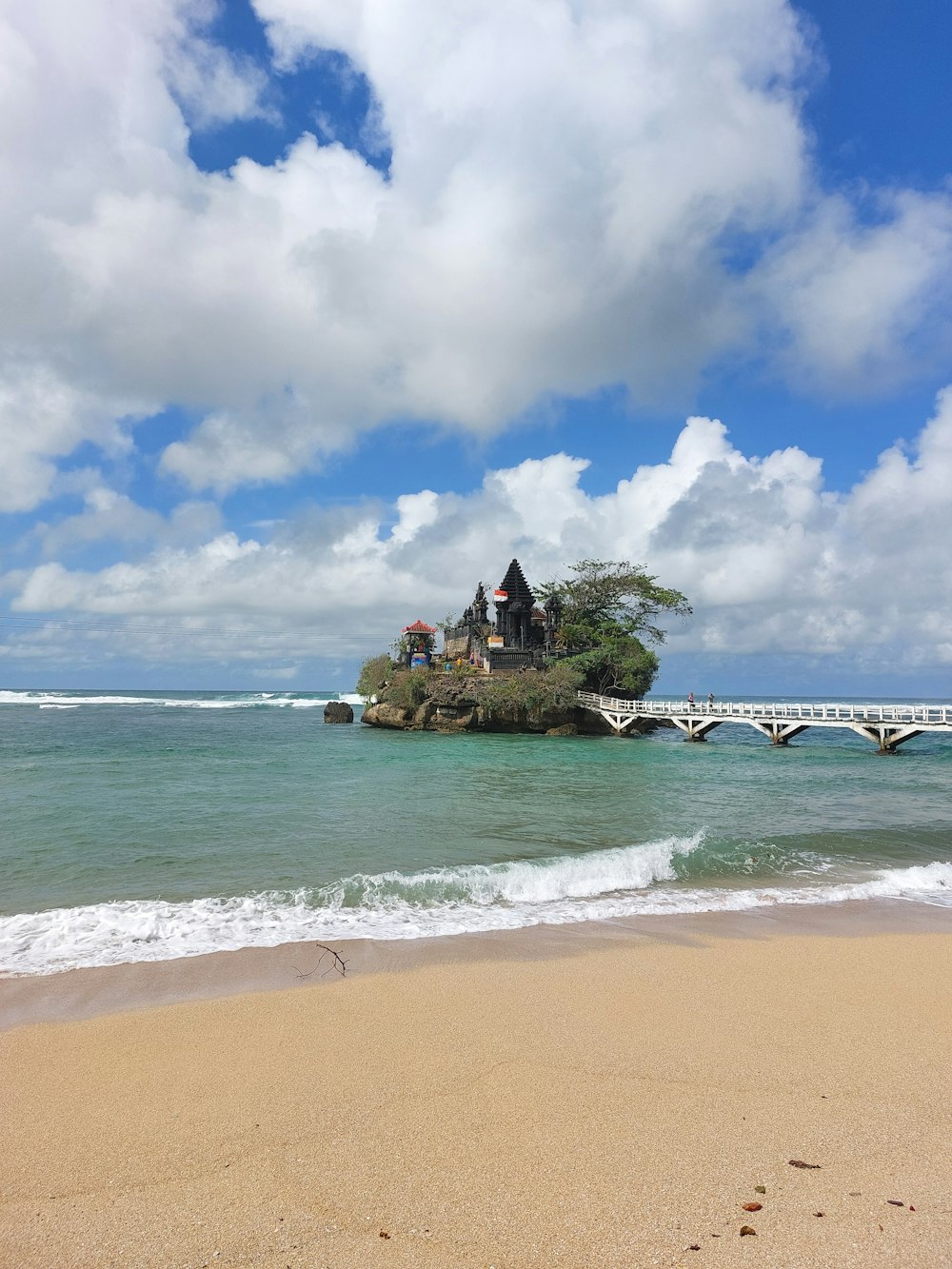 a beach with a small island with a bridge and a building on it