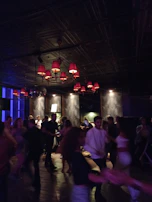 A dimly lit dance floor filled with people lost in the rhythm, shadows blending with deep charcoal walls.