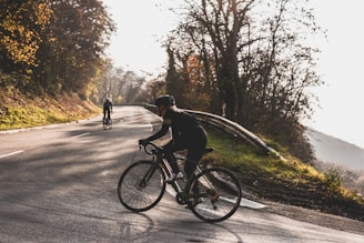 Cyclist training intensely on a road, sunlight breaking through trees.