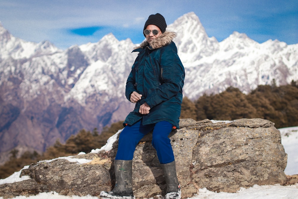 a person standing on a rock with snow and mountains in the background